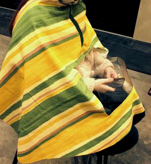 Personne assise de profile, vêtue d'une cape de pluie à rayures jaune et verte avec une poche transparente sous laquelle elle utilise son téléphone.