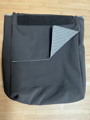 Sacoche noire rectangulaire avec abattant sur le dessus dont le coin est retourné pour voir la doublure, et avec un bande de velcro